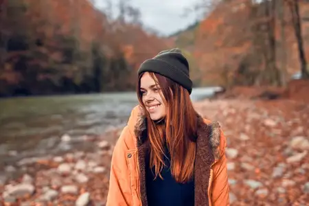 Жизнерадостная женщина-туристка в куртке в осеннем лесу у реки на фоне природы