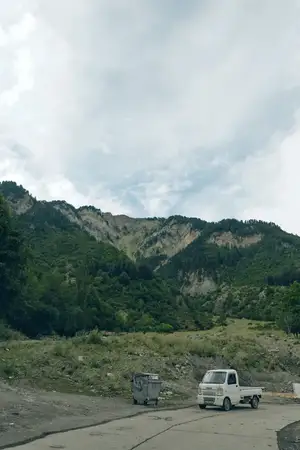 Горный пейзаж с одиноким грузовиком на извилистой дороге, обнаженной скалой и открытым небом, передающий ощущение уединения, путешествия и сельских просторов