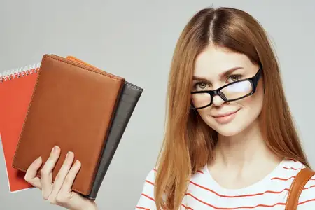 Студентка с блокнотом и в очках на светлом фоне, кадрированный вид