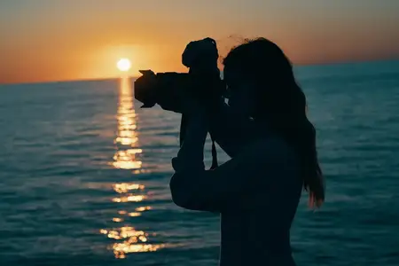 Женщина-фотограф с камерой на закате у моря на фоне природного пейзажа
