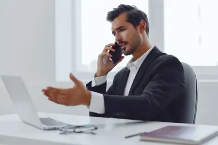 Улыбающийся мужчина, умный, пользуется беспроводным интернетом, сидит с ноутбуком и телефоном, мобильное устройство, кавказец, рабочее место, предприниматель, офисный работник, бизнесмен…