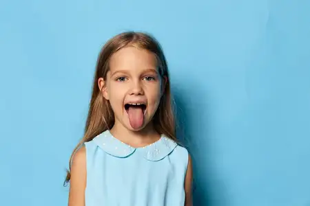Игривая маленькая девочка показывает язык на голубом фоне с большим свободным пространством