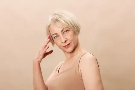 Светловолосая женщина средних лет с короткими волосами и в бежевом топе без рукавов уверенно смотрит в камеру