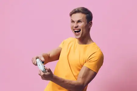 Счастливый мужчина в повседневной желтой футболке наслаждается игровой сессией, держит геймпад с восторгом и смехом
