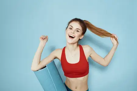 Спортивная женщина держит в руках тренировочный коврик