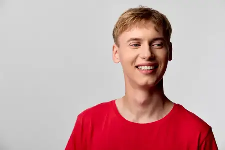 Счастливый мужчина в красной футболке с дружелюбной улыбкой, студийное освещение подчеркивает теплое, приподнятое настроение и непринужденную позу, идеально подходит для маркетинга, социальных сетей…