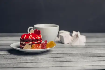 Чашка чая и красное пирожное на блюдце, сладости, десерт на деревянном фоне