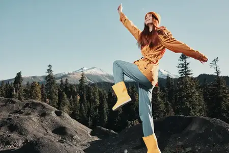 Женщина-туристка в жёлтом дождевике улыбается, показывая зубы, излучая счастье и смех