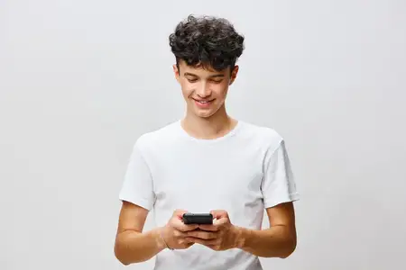 Улыбающийся молодой человек взаимодействует со своим смартфоном, одетый в простую белую футболку