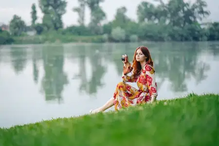 Женщина в платье с фотоаппаратом на природе занимается своим хобби — фотографией