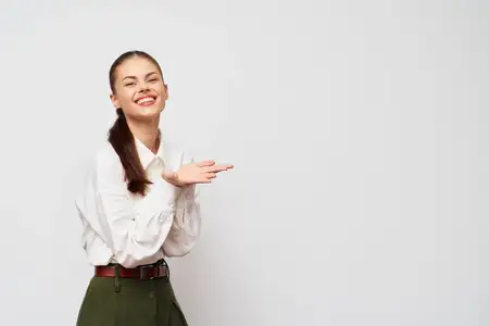 Весёлая молодая женщина в белой блузке и зелёной юбке стоит на фоне светло-серого фона