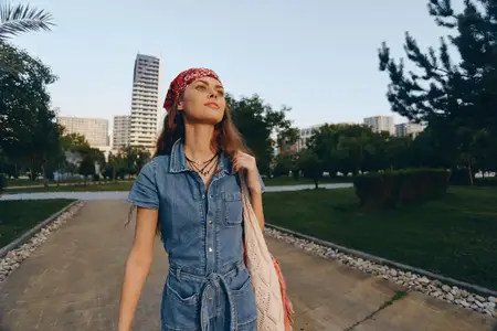 Женщина в стиле лайфстайл, одетая в современный бохо-вестерн деним уличного стиля и красную бандану, идет по городской дорожке на закате с теплой пленочной цветокоррекцией