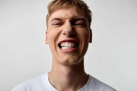 Крупный план улыбающегося мужского лица с оскалом зубов, сильным выражением, энергичной эмоцией, необузданной жизненной силой и ярким настроением в студийной обстановке