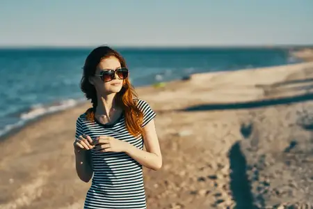 Красивая женщина в футболке и очках на пляже у моря в горах