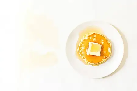 Визуально привлекательная стопка пышных блинов, украшенная кусочком масла и золотистым сиропом, идеально подходит для завтрака, бранча или фуд-фотографии, выполненная в минималистичном стиле