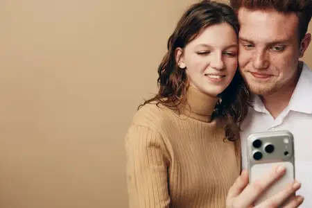 Улыбающиеся молодые мужчина и женщина в повседневной одежде держат смартфон для селфи