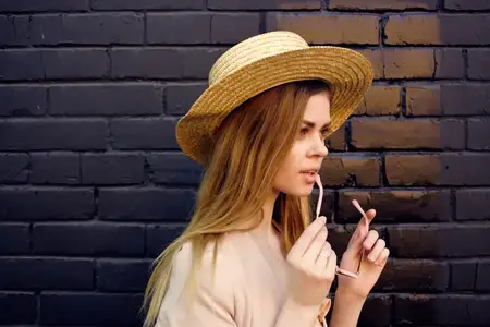 Симпатичная женщина на улице в шляпе и очках позирует на фоне черной кирпичной стены