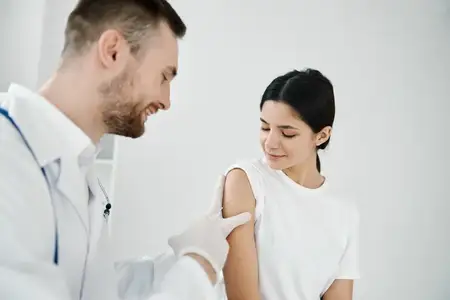 Врач со стетоскопом делает инъекцию в плечо пациентке на светлом фоне
