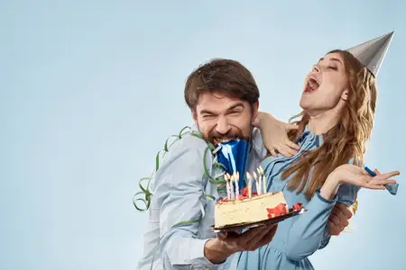 Мужчина и женщина в праздничных колпаках на синем фоне с тортом и свечами