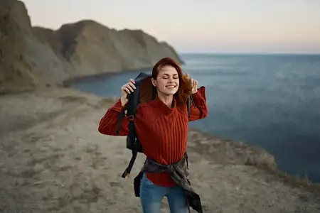 Женщина на фоне осеннего пейзажа: горы, море, пляж, рюкзак