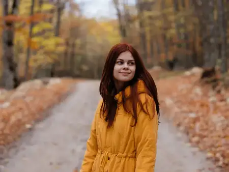 Женщина в жёлтой куртке гуляет по осеннему лесу