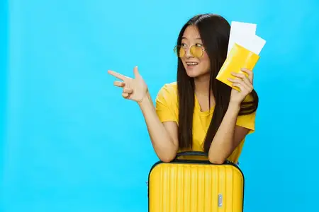Азиатская женщина путешествует с желтым чемоданом, билетами и паспортом в руках