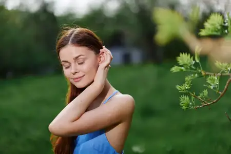 Портрет молодой женщины с красивой улыбкой, обнажающей зубы, на фоне деревьев весной в солнечный день