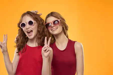 Счастливые сёстры в красных платьях на жёлтом фоне веселятся и жестикулируют