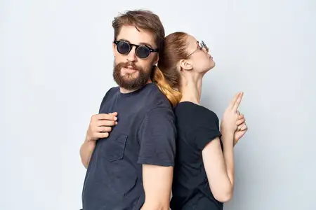 Модные мужчина и женщина в чёрных футболках и солнцезащитных очках позируют на светлом фоне