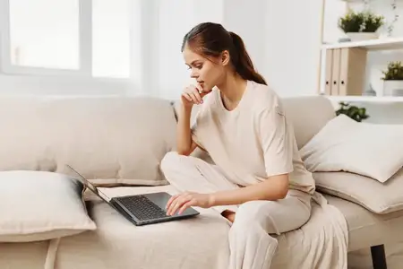 Успешная женщина работает из дома: улыбающаяся женщина печатает на ноутбуке в уютной гостиной