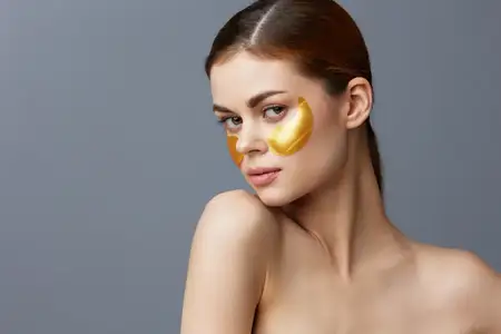 Молодая женщина с золотыми патчами на чистой коже улыбается и позирует крупным планом