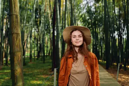 Портрет женщины в шляпе на тропинке в бамбуковом лесу с улыбкой