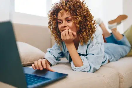 Улыбающаяся женщина работает за ноутбуком в уютном, современном домашнем офисе