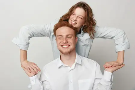 Улыбающиеся молодые мужчина и женщина в белых рубашках наслаждаются игривым моментом вместе на однотонном фоне