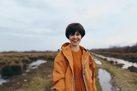Портрет женщины на открытом воздухе, оранжевая куртка, теплая улыбка и короткие волосы