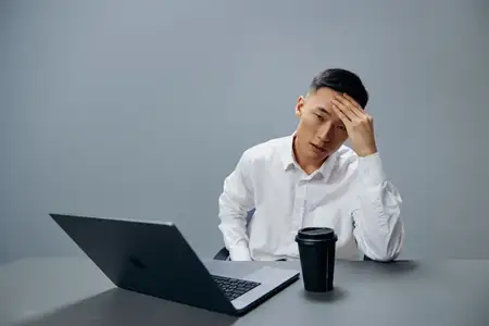 Усталость работника, эмоции, ноутбук, работа, кофе на рабочем столе на сером фоне