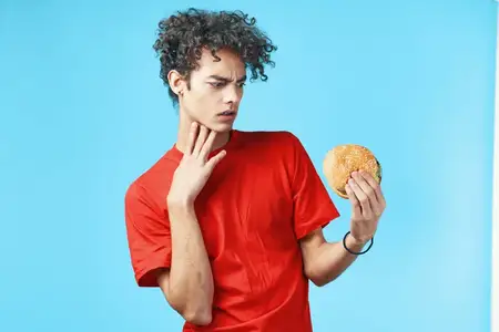 Парень с кудрявыми волосами в красной футболке, гамбургер, фастфуд, синий фон