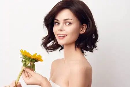 Молодая женщина держит подсолнух на белом фоне