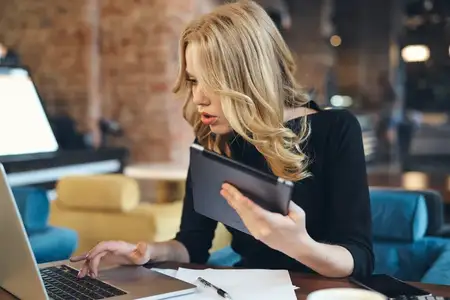 Женщина с ноутбуком в кафе, фрилансер за работой, рядом планшет и чашка кофе