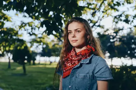 Женщина в стиле лайфстайл, одетая в современный бохо-вестерн деним стритстайл, стоит на открытом воздухе под деревьями, залитая тёплым плёночным светом, что создаёт расслабленную и естественную…