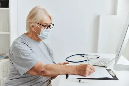 Пожилая женщина сидит за столом, записываясь на вакцинацию