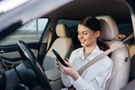 Женщина в машине пользуется телефоном, улыбается и взаимодействует со своим устройством