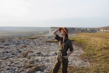Женщина в шляпе стоит на вершине холма, на заднем плане открывается вид на долину во время путешествия-приключения в модной поездке