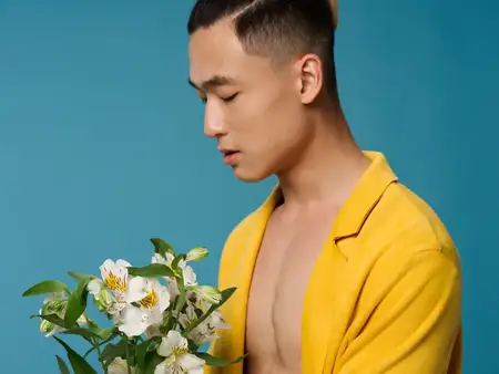 Романтичный мужчина в жёлтом пальто на голый торс, держащий в руке букет цветов и праздничное настроение