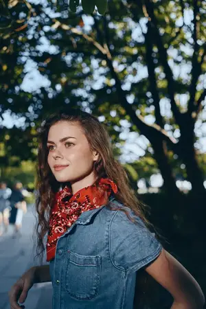 Женщина в стиле жизни, одетая в современный бохо-вестерн джинсовый стритстайл с яркой красной банданой, стоит на открытом воздухе с пятнистым солнечным светом и зелёным лиственным фоном
