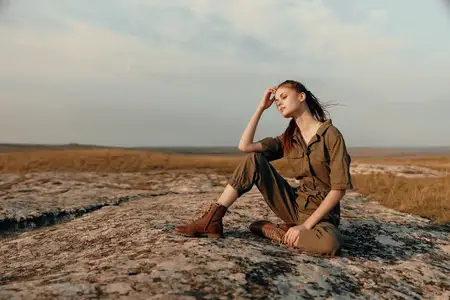 Женщина размышляет о жизни на отдаленном камне посреди бескрайнего поля зеленой травы