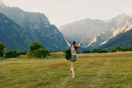 Яркая outdoor-сцена показывает женщину, наслаждающуюся природой: широкий луг, атмосфера похода, открытое небо, теплые цвета, неторопливый темп, простой приключенческий образ жизни