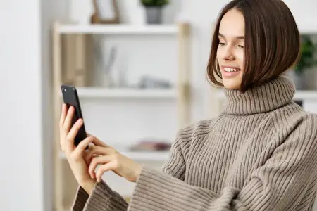 Женщина европеоидной расы сидит дома, делает селфи на смартфон