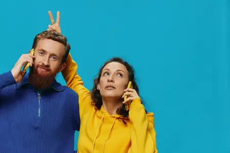 Весёлая пара — женщина и мужчина — с телефонами в руках, у них кривые улыбки, они радостны на голубом фоне