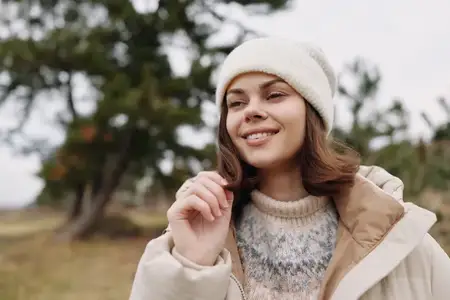 Уличная сцена с улыбающейся женщиной в повседневной одежде: свитер и куртка, вязаная шапка, расслабленное настроение и естественная сезонная атмосфера